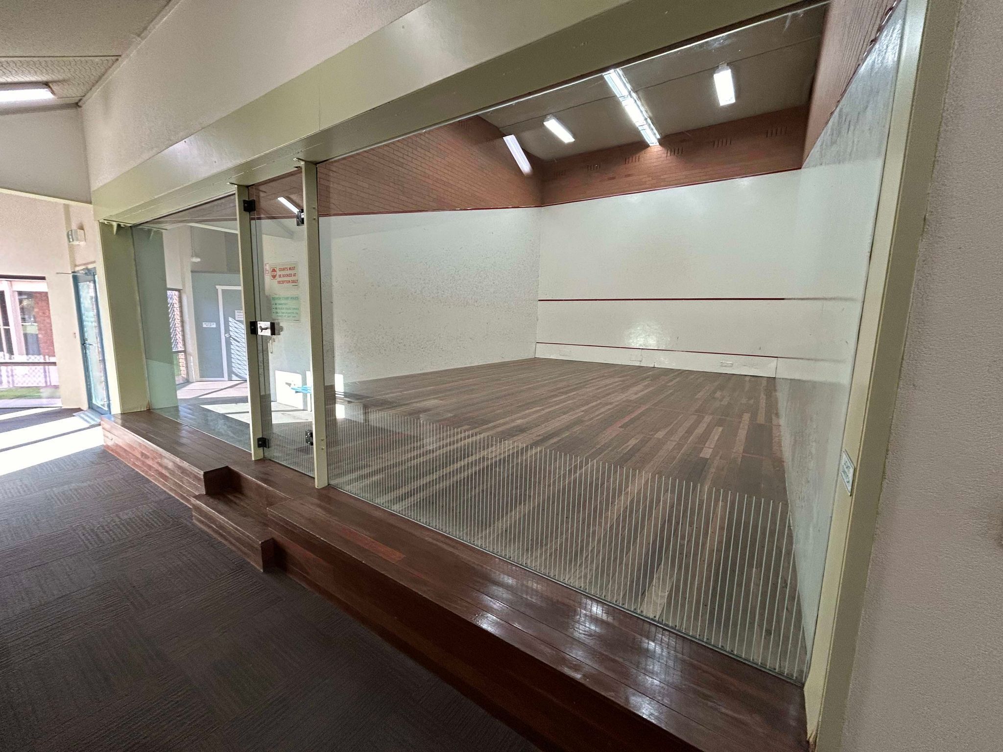 A room with a large glass partition, a wooden floor, and a bench along the wall.