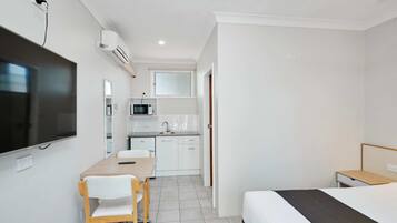 Habitación de hotel pequeña con cama, escritorio con silla, televisor en la pared, microondas y kitchenette.