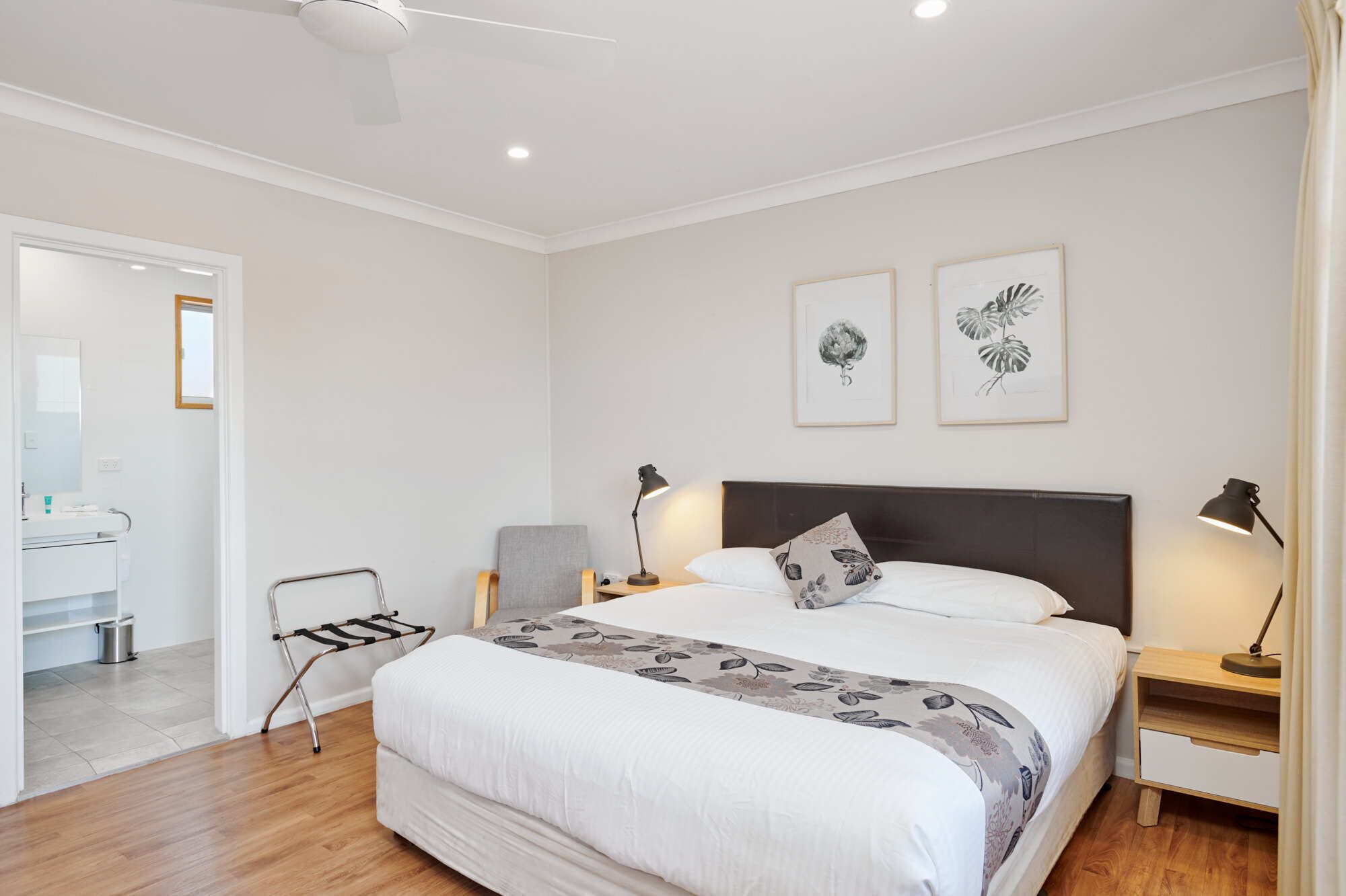 Une chambre à coucher avec un grand lit, deux tables de chevet avec des lampes, une chaise et une porte donnant sur une salle de bain.
