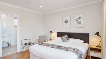 Une chambre à coucher avec un grand lit, deux tables de chevet avec des lampes, une chaise et une porte donnant sur une salle de bain.