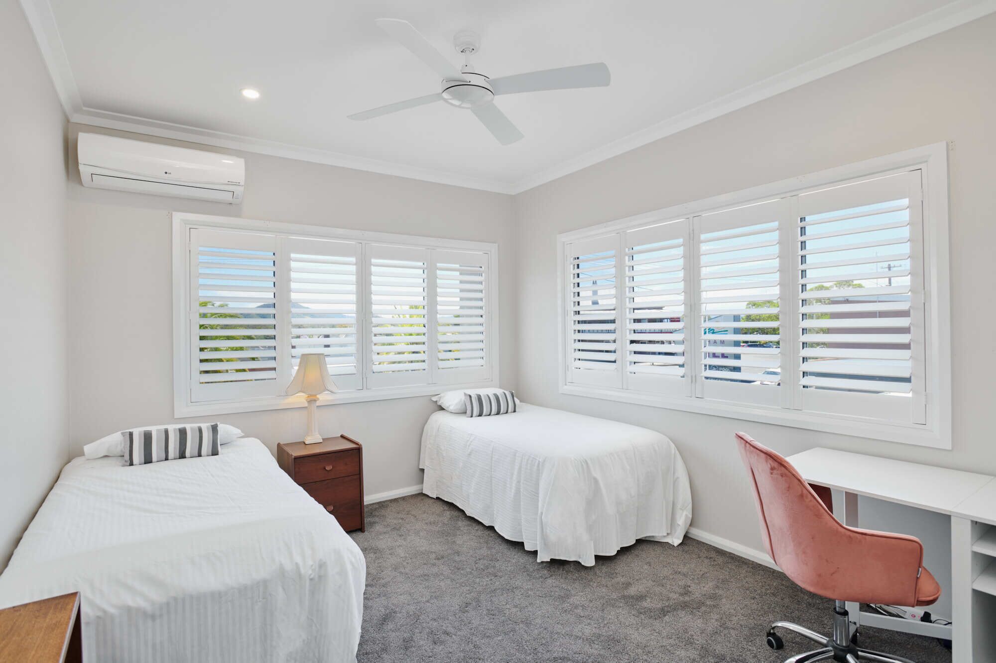 A room with two beds, a desk, a chair, and a ceiling fan.