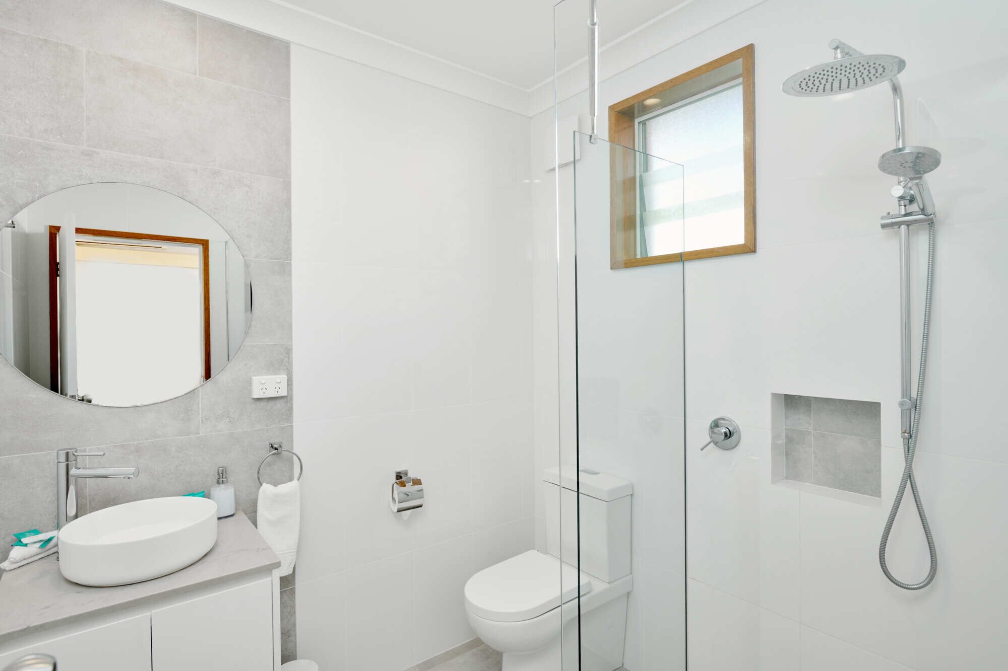 A modern bathroom with a round mirror, a sink, a toilet, and a shower.