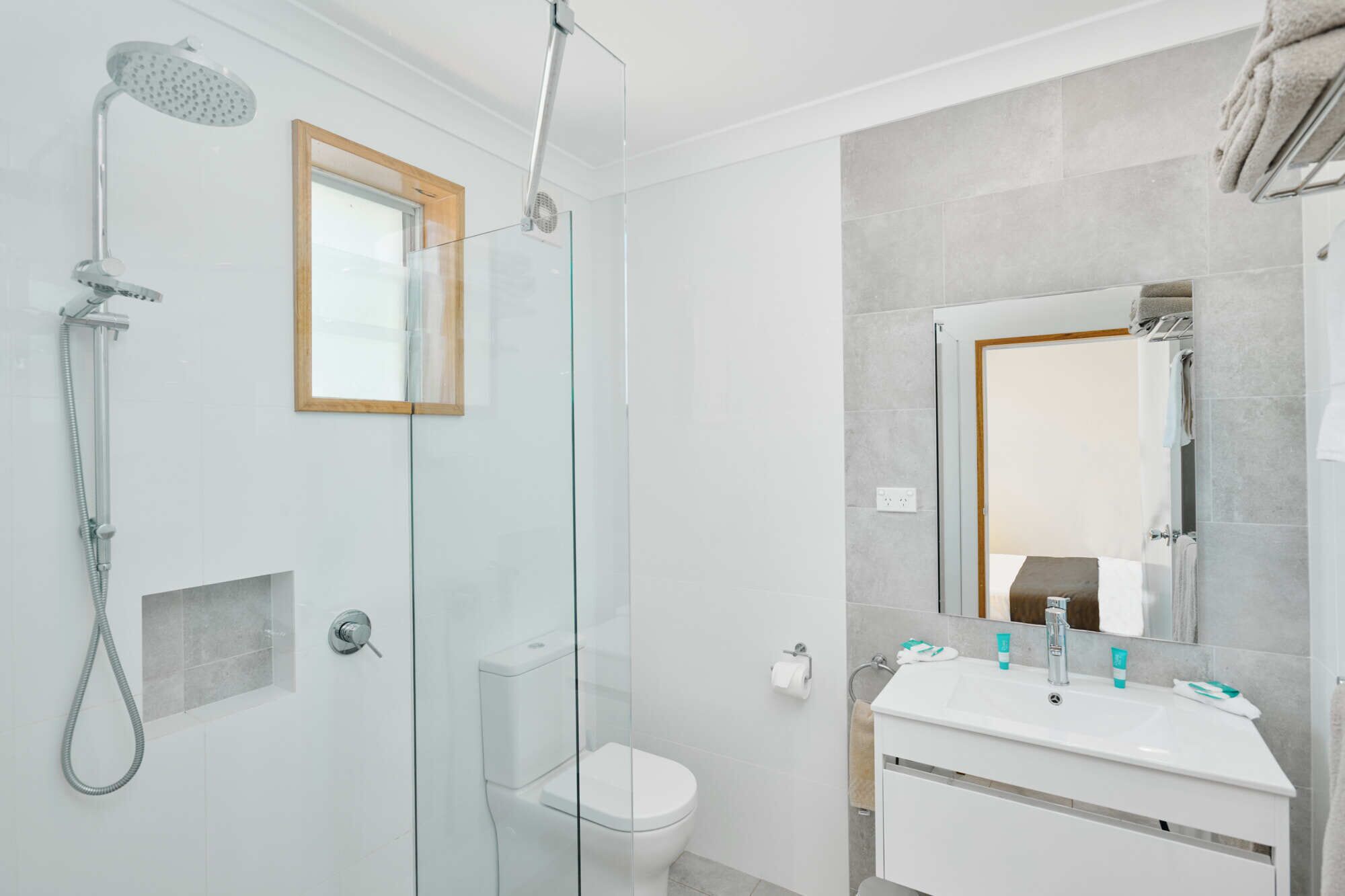Un baño moderno con ducha de vidrio, inodoro y lavamanos con espejo.