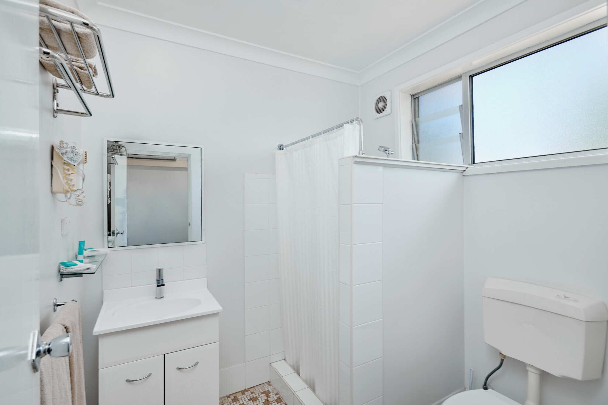 Un baño pequeño y blanco con ducha, inodoro y lavabo.