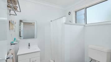 Un baño pequeño y blanco con ducha, inodoro y lavabo.