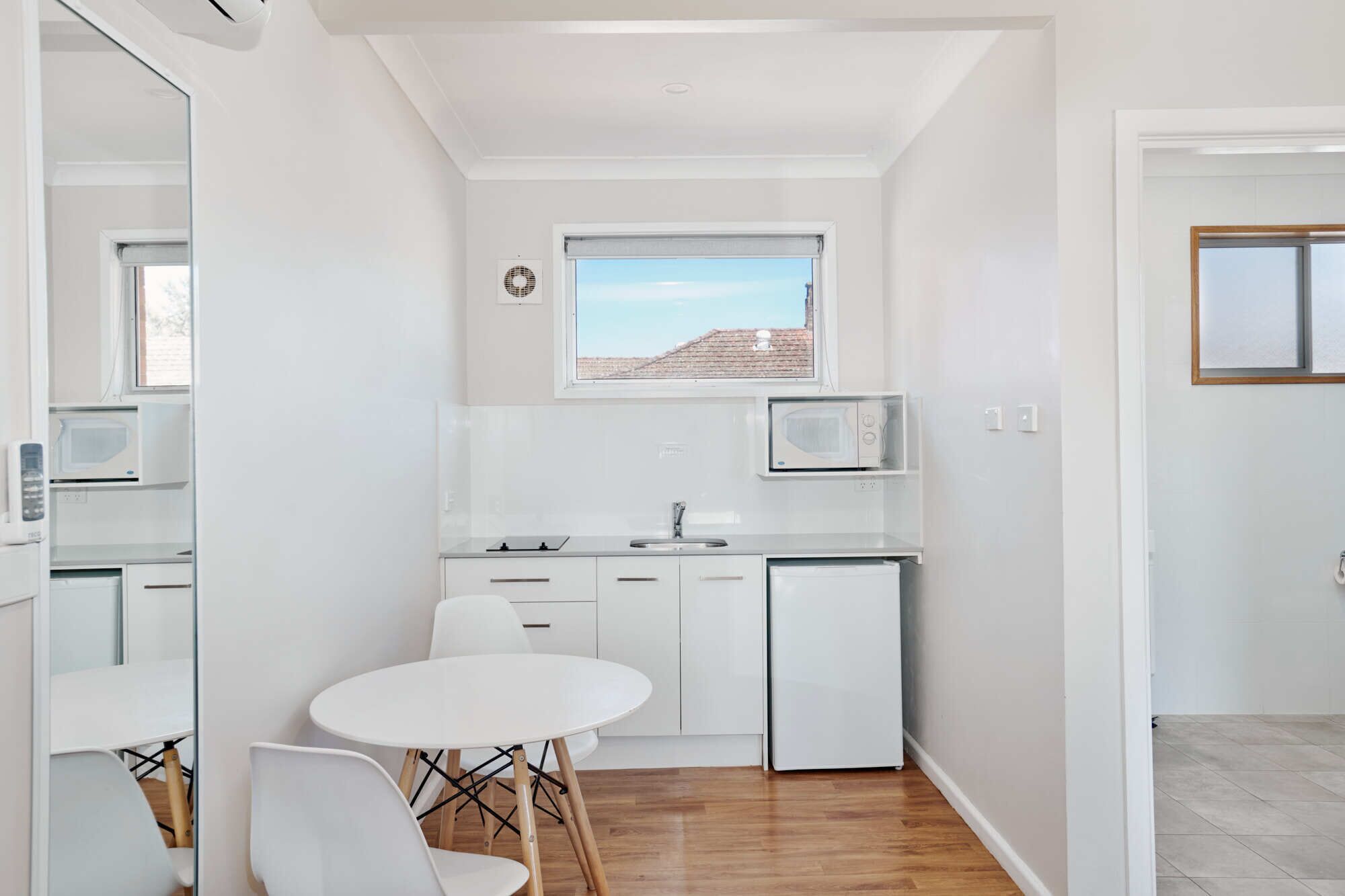 A compact kitchen with white cabinets, a small refrigerator, a microwave, and a dining area with a white table and chairs.