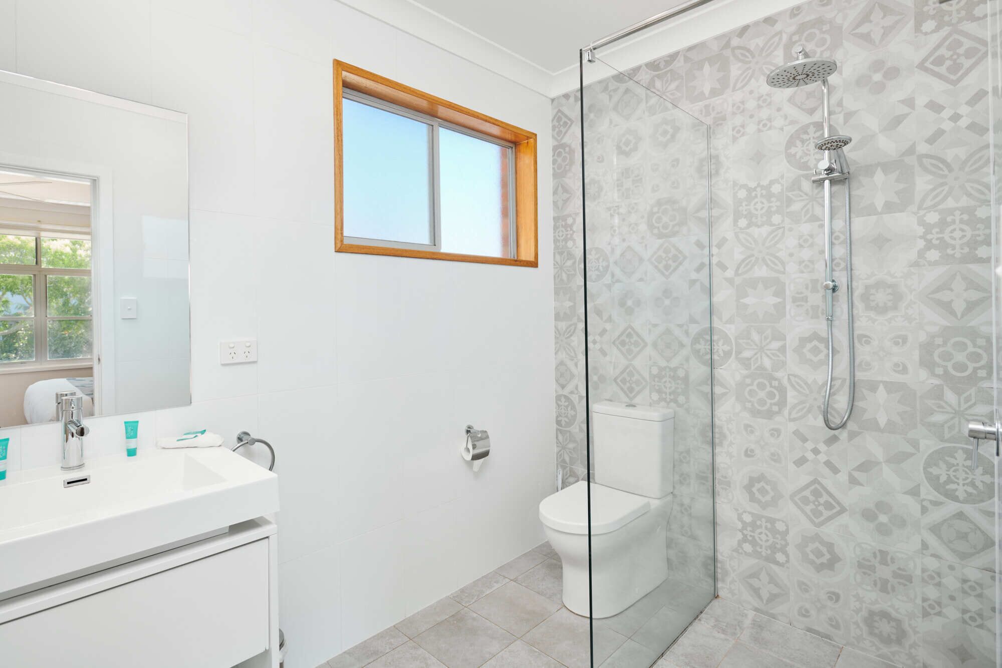 A modern bathroom with a glass shower enclosure, a white toilet, and a sink with a mirror.