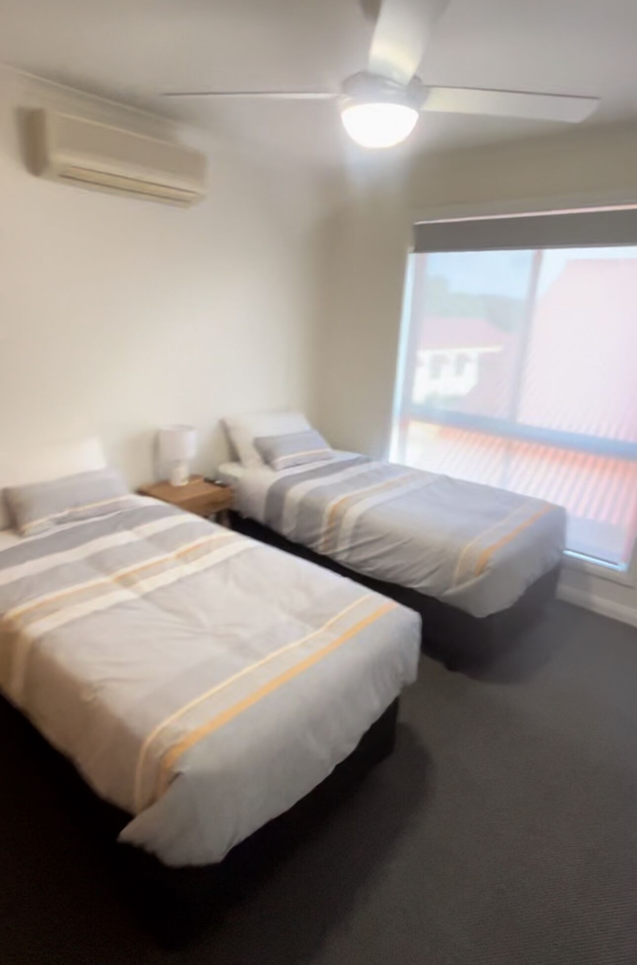 A room with two beds, a ceiling fan, and a large window.