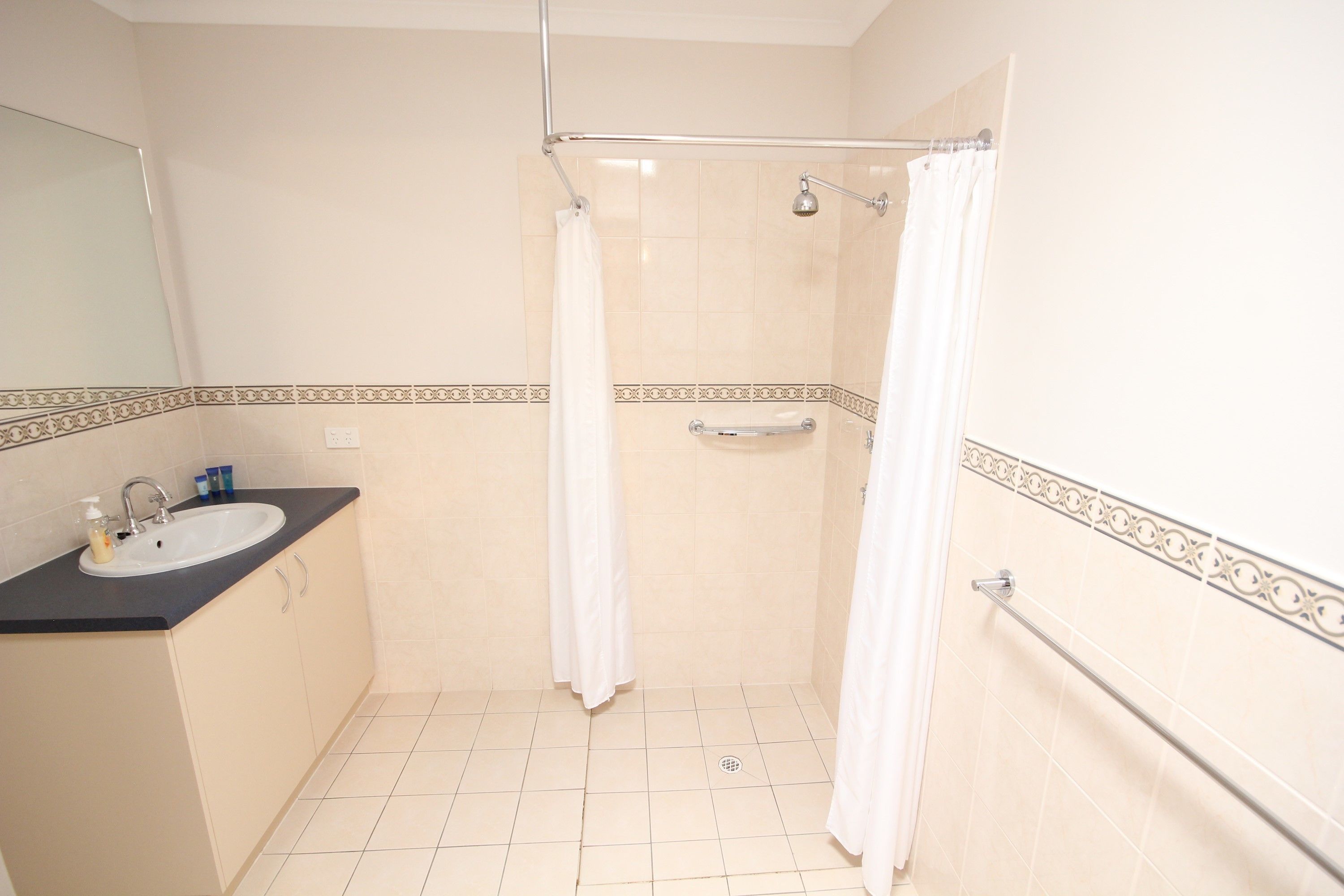 A bathroom with a sink, mirror, shower, and tiled floor.