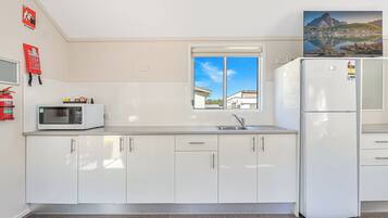 A kitchen with white cabinets, a microwave, a refrigerator, a window, and a fire extinguisher.