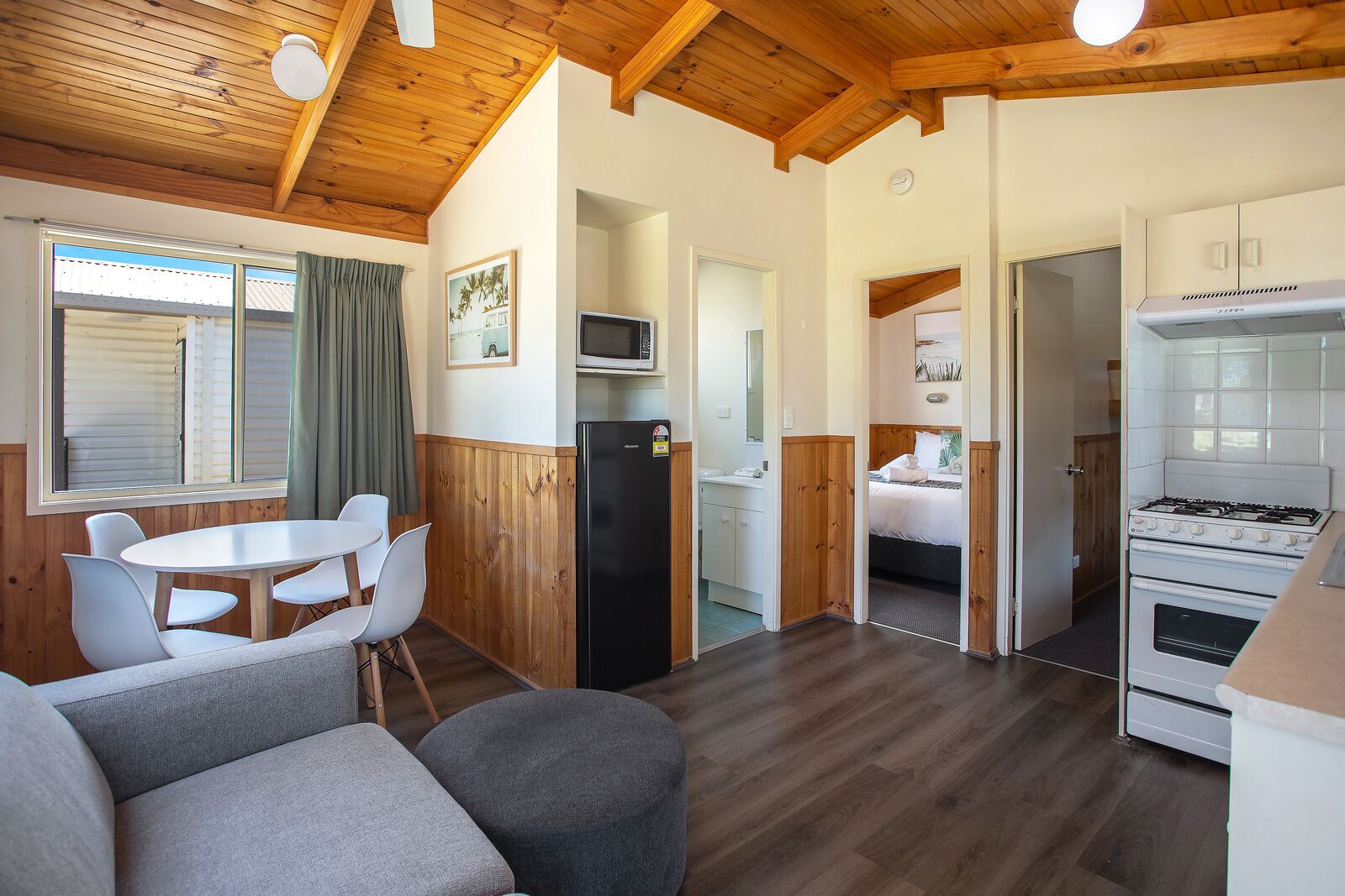 Habitación de hotel compacta con kitchenette, comedor con mesa y sillas, y una cama.