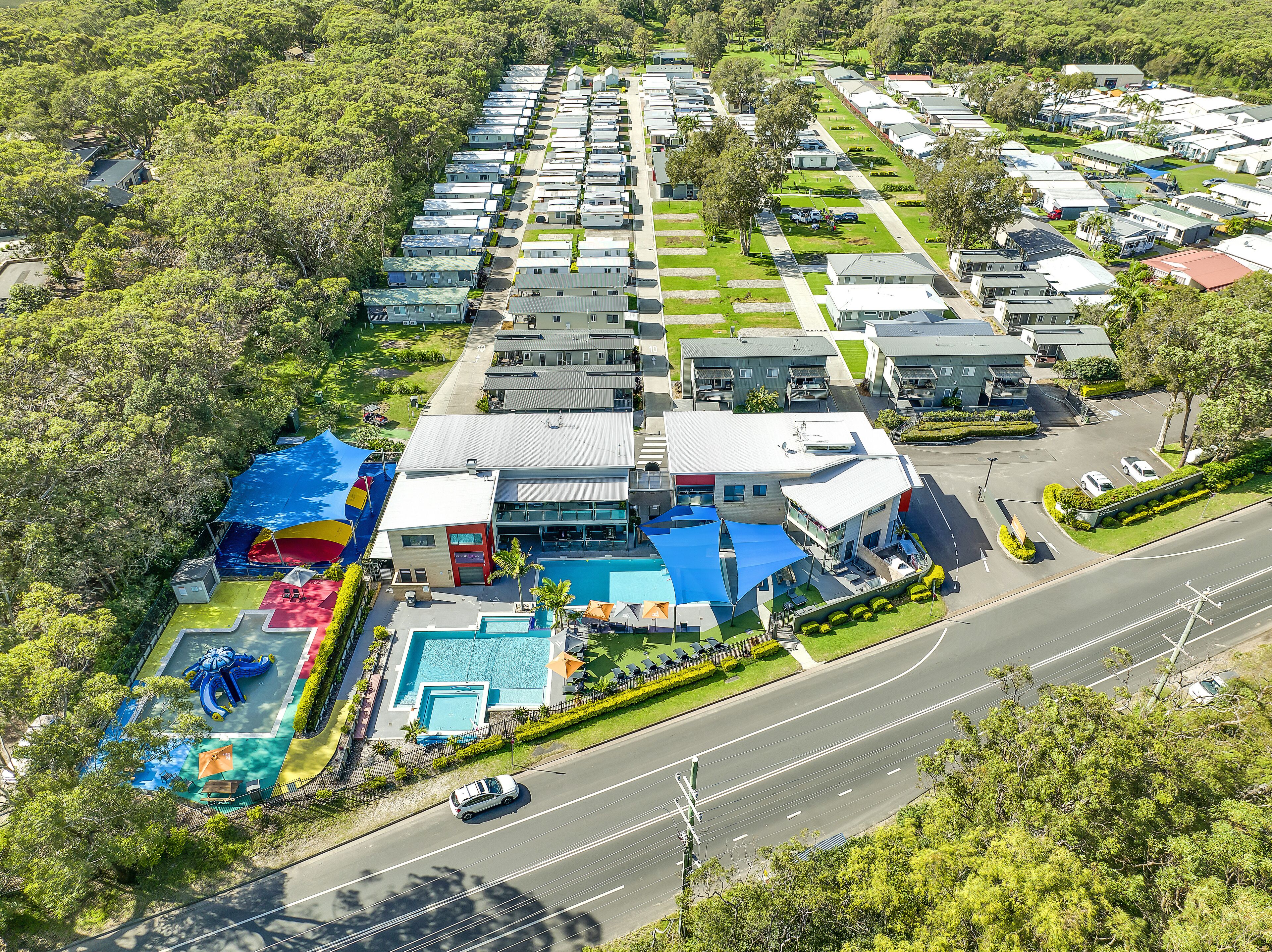 An aerial view of a residential area with rows of houses, a swimming pool, and a road.