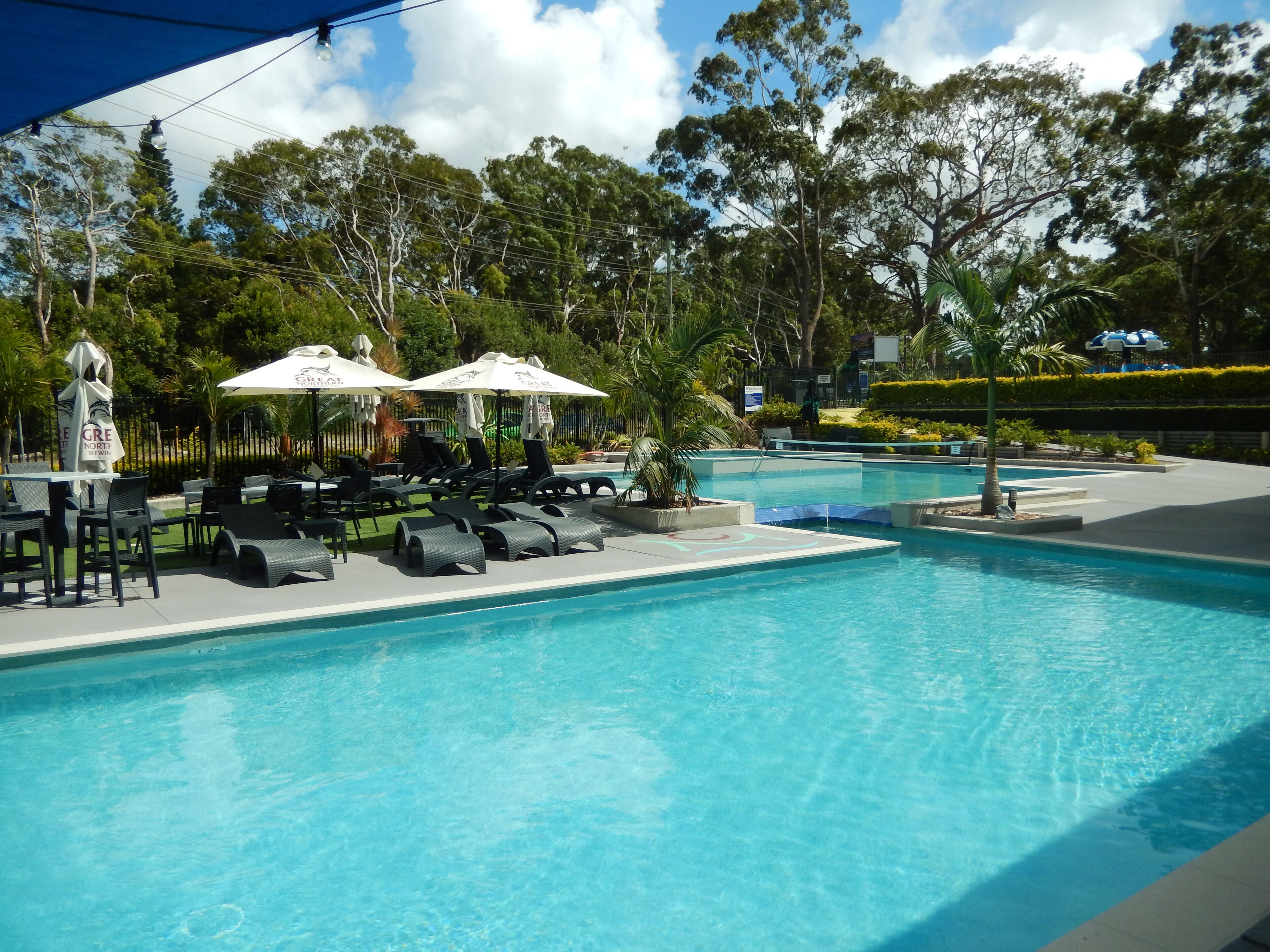 A swimming pool with lounge chairs and umbrellas, surrounded by trees and a fence.