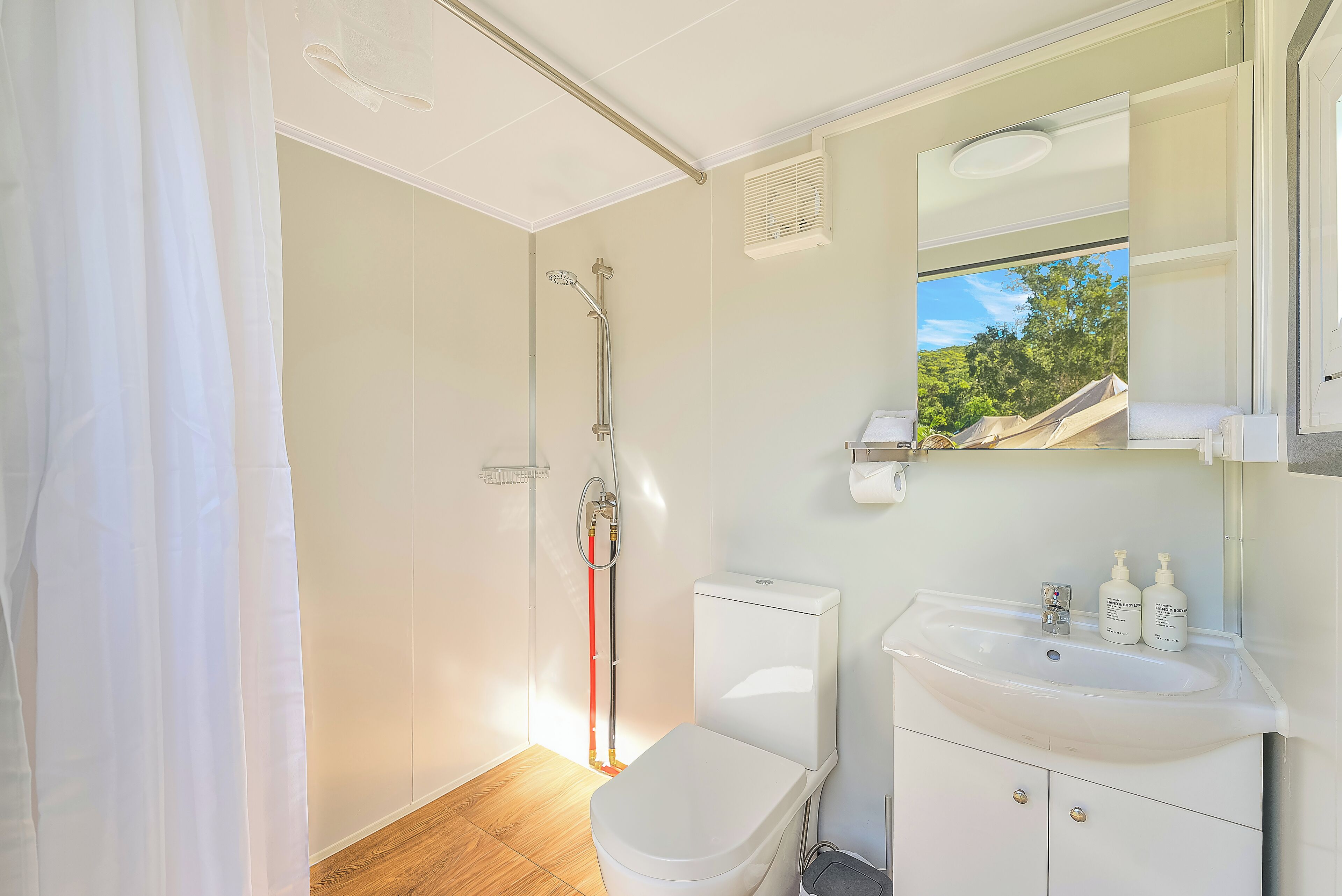 Une salle de bain équipée d’une douche, de toilettes, d’un lavabo et d’une fenêtre donnant sur les arbres.