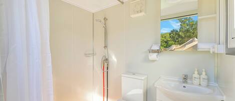 Une salle de bain équipée d’une douche, de toilettes, d’un lavabo et d’une fenêtre donnant sur les arbres.