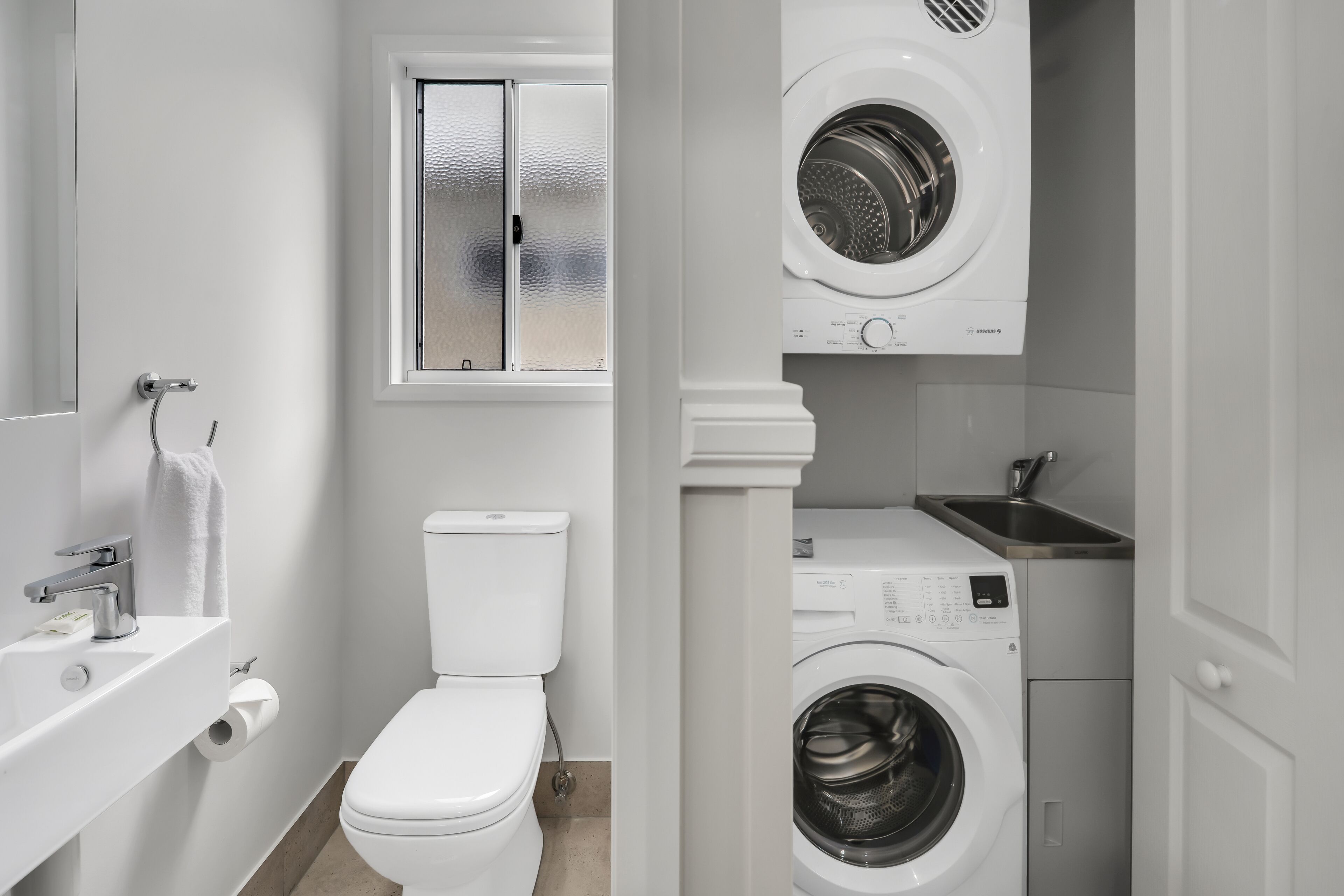 Ein kleines, modernes Badezimmer mit Toilette, Waschbecken und zwei Waschmaschinen.