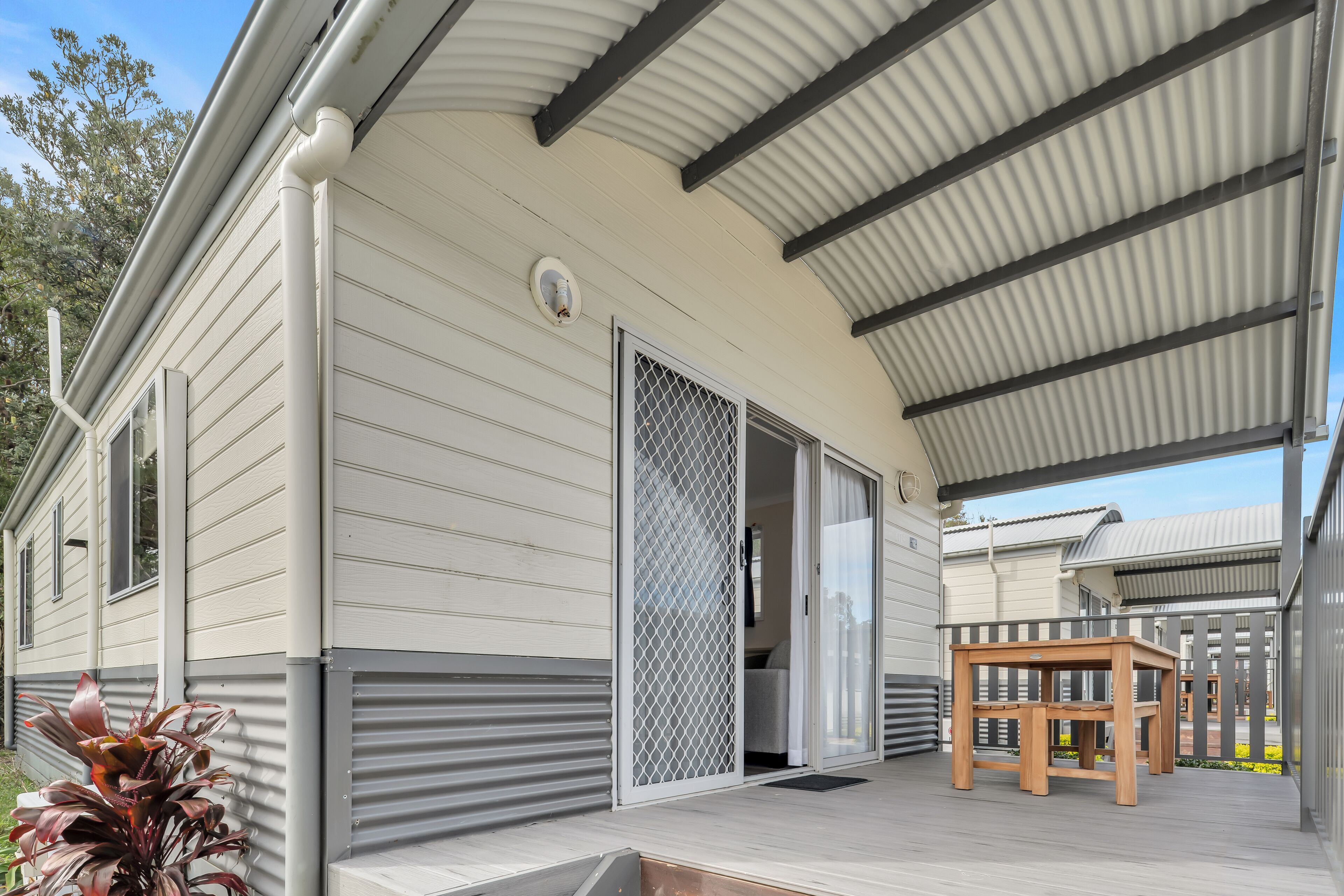 A covered outdoor area with a wooden table and chairs, a sliding glass door, and a metal railing.