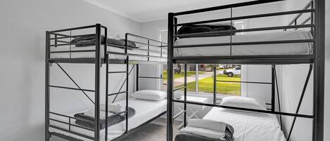 A room with two bunk beds, white walls, and a window with a view of a green lawn and parked cars.