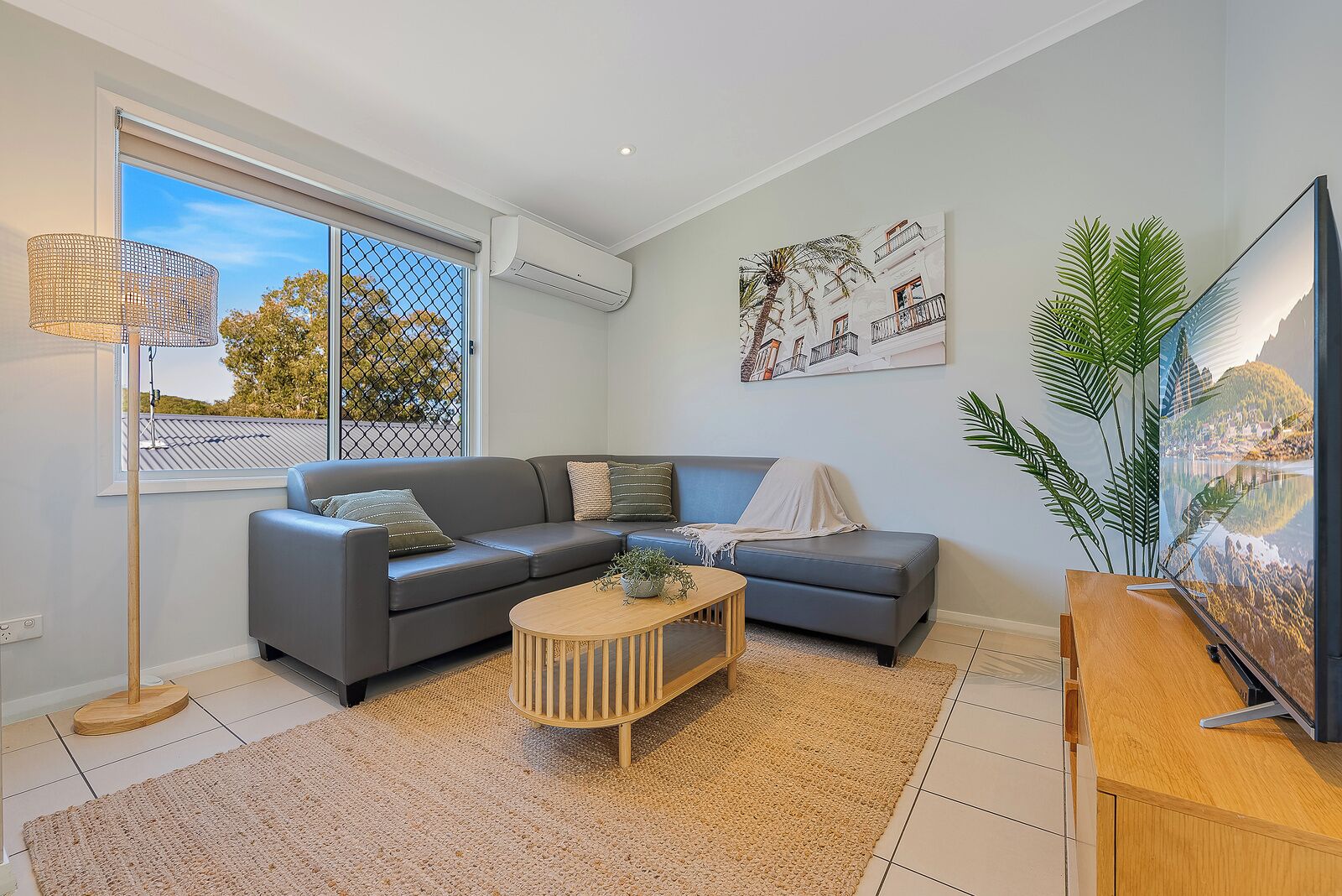 A modern living room with a grey sofa, a wooden coffee table, and a large window with a view of trees.