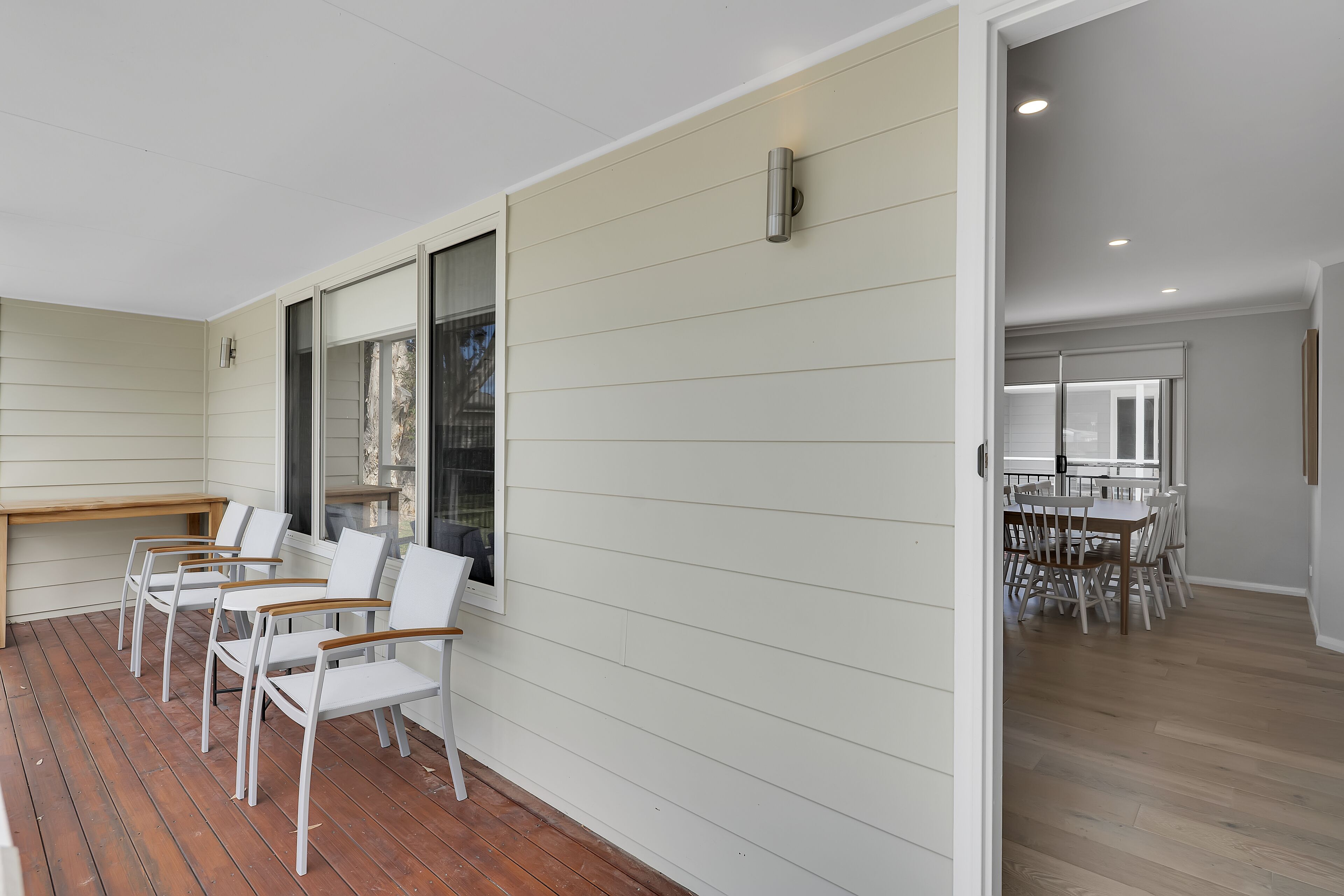 A modern interior with a wooden deck, white chairs, and a dining area with a large table and chairs.