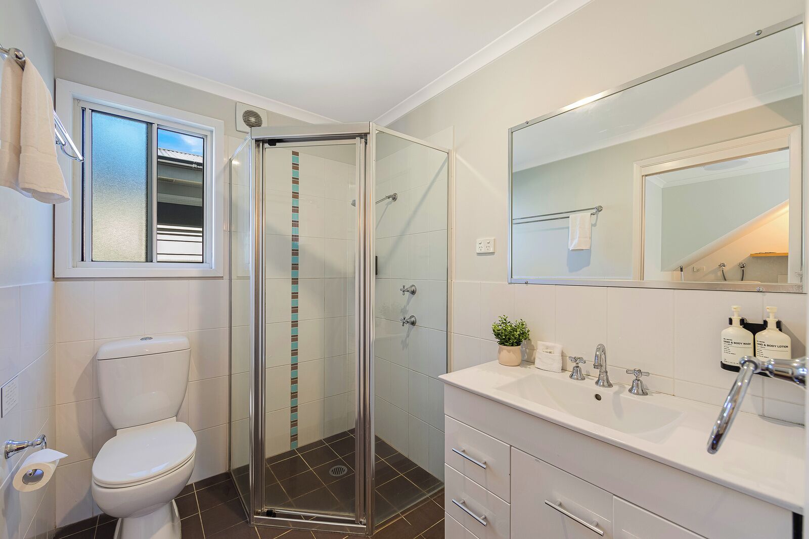 Un baño moderno con cabina de ducha de vidrio, inodoro, lavabo con espejo y artículos de aseo.