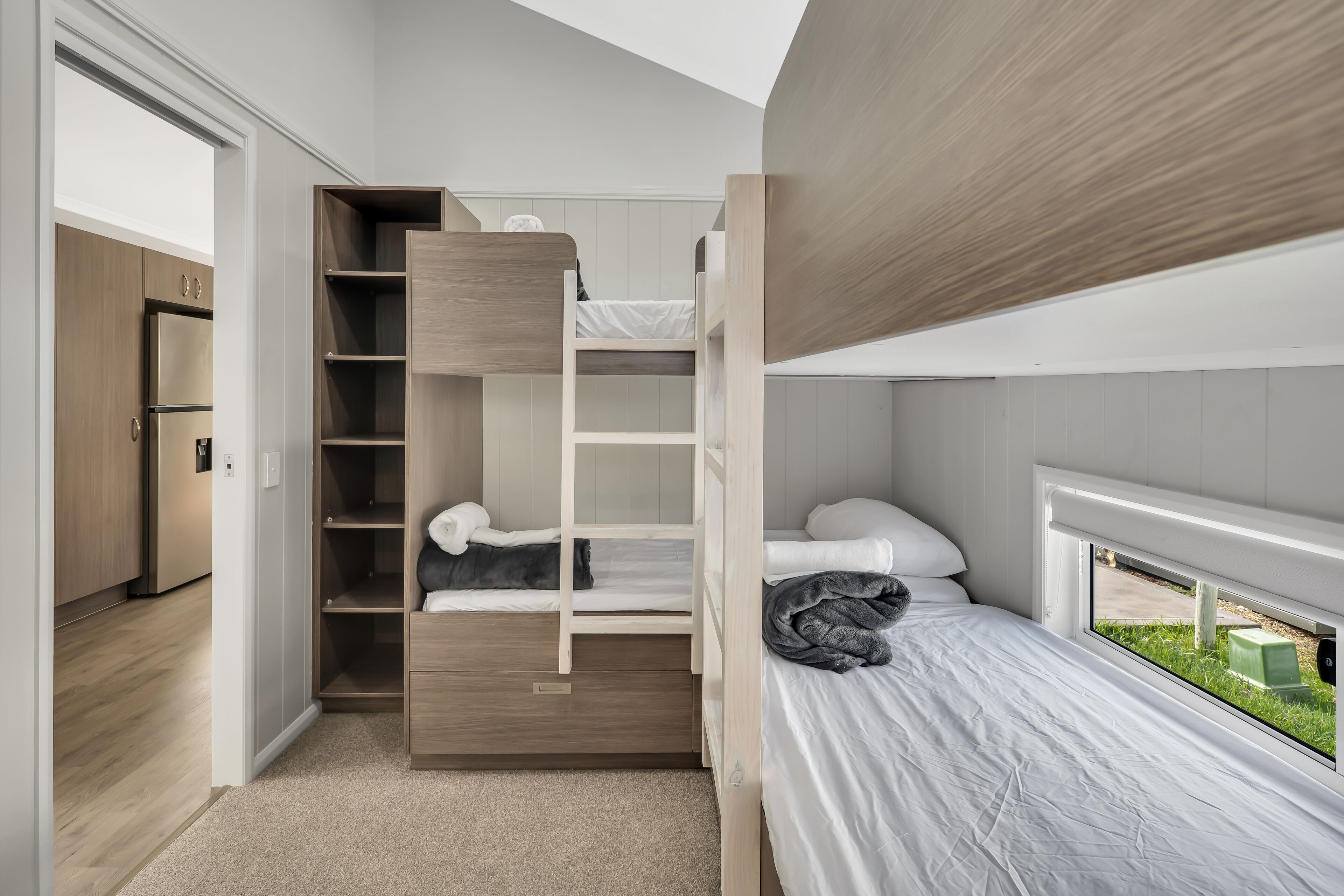 A compact bedroom with a bunk bed, a small closet, and a window with a view of the outdoors.