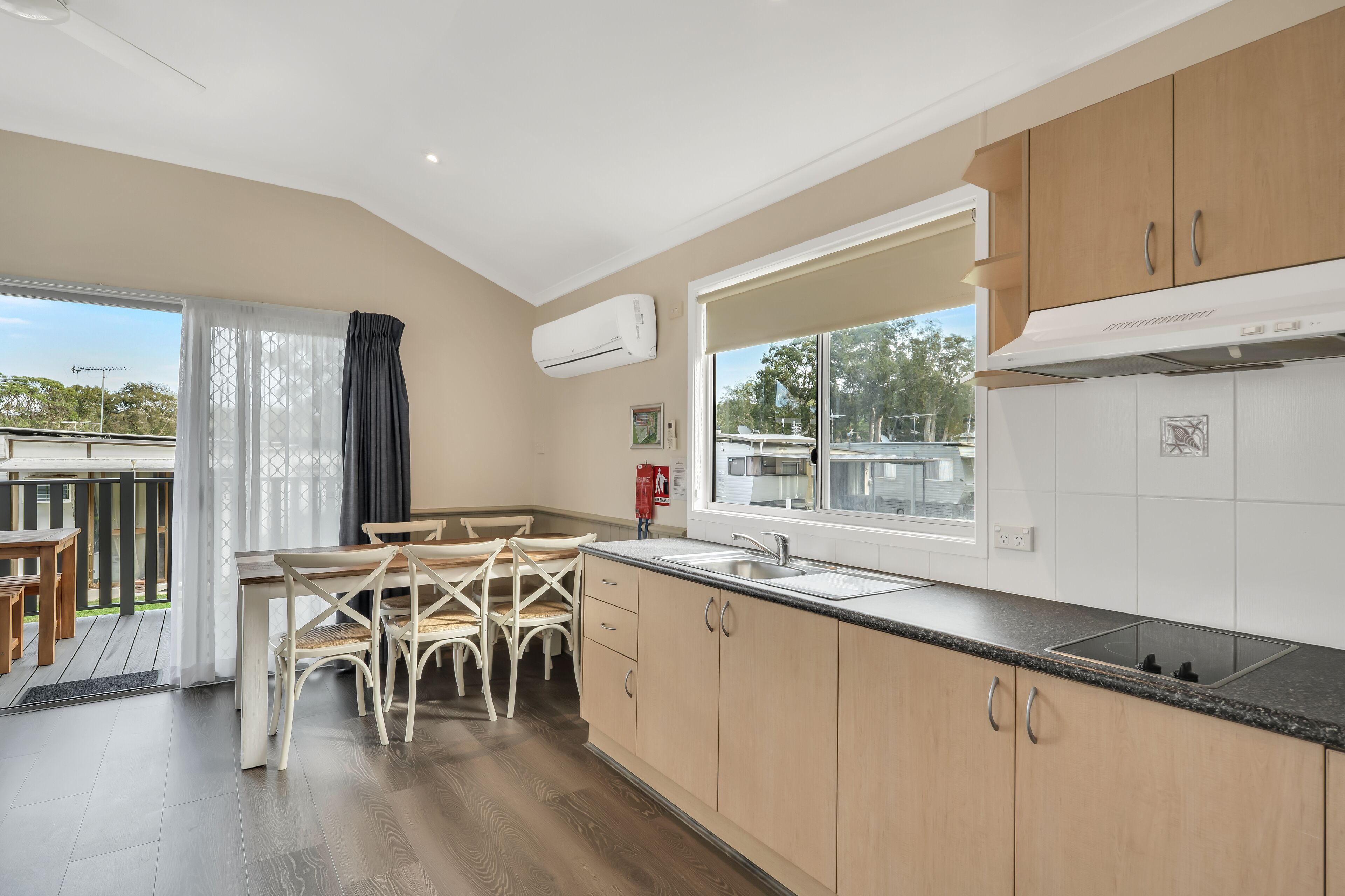 A modern kitchen with wooden cabinets, a large window, and a dining area with chairs.