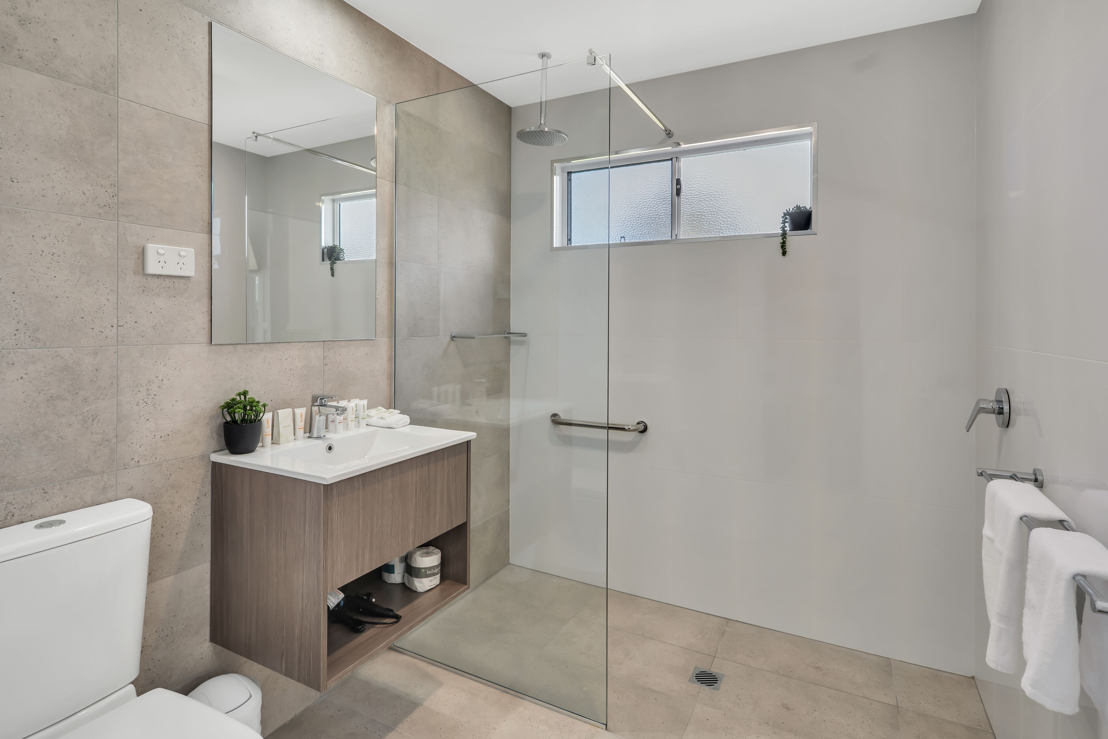 Une salle de bain moderne avec une douche à parois de verre, un meuble-lavabo en bois et un grand miroir.