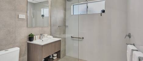 Une salle de bain moderne avec une douche à parois de verre, un meuble-lavabo en bois et un grand miroir.