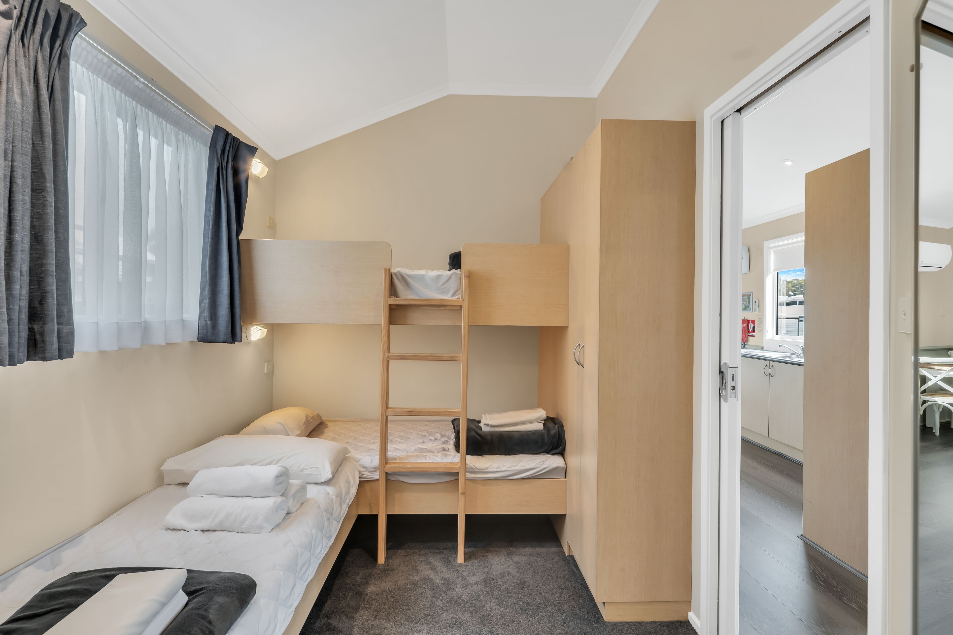 A compact room with bunk beds, a small desk, and a window with curtains.