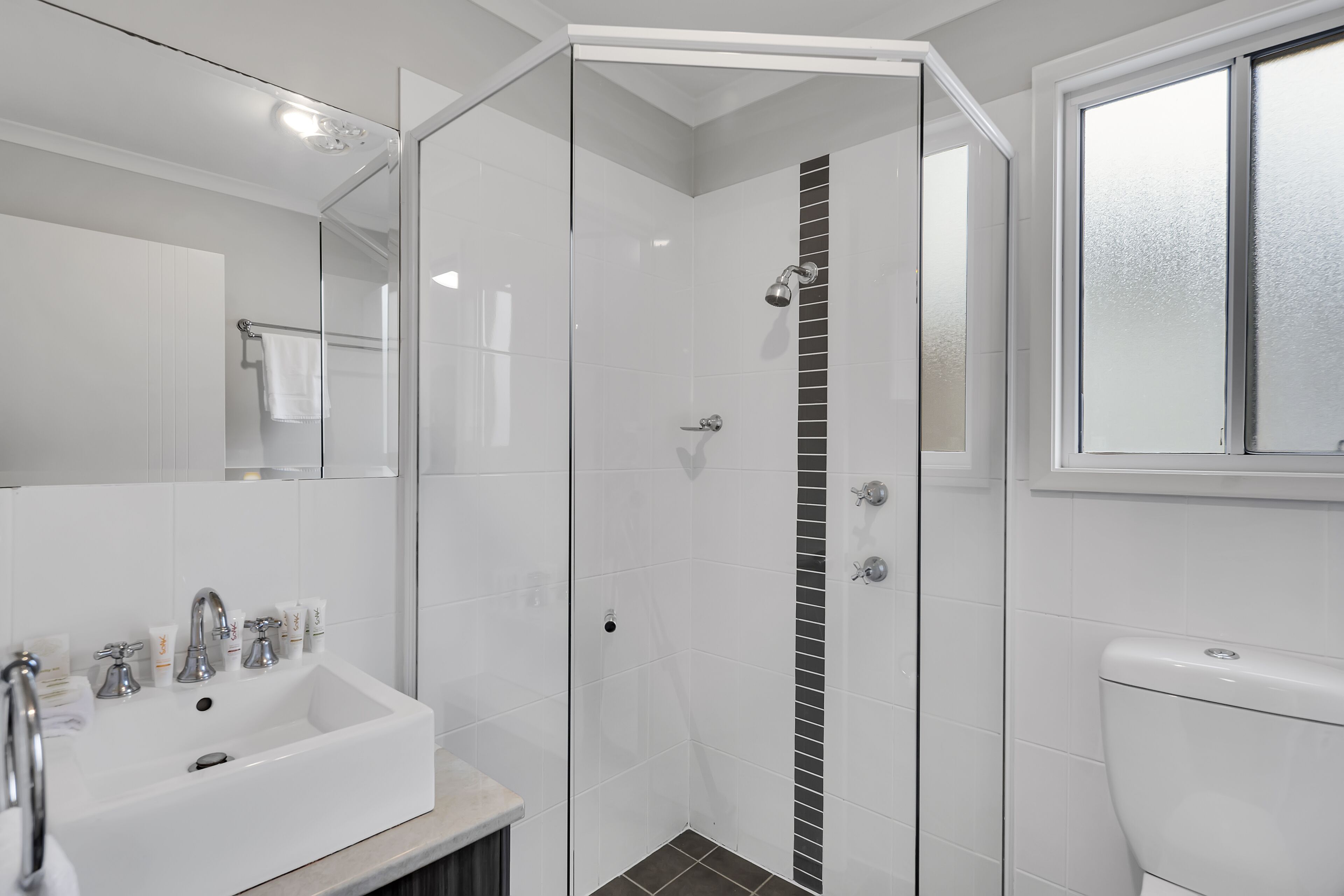 A modern bathroom with a glass-enclosed shower, a white sink with multiple faucets, and a toilet.