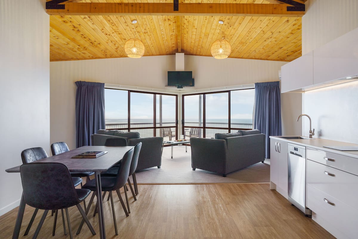 A modern kitchen with a large window, wooden ceiling, and a dining area with a view.