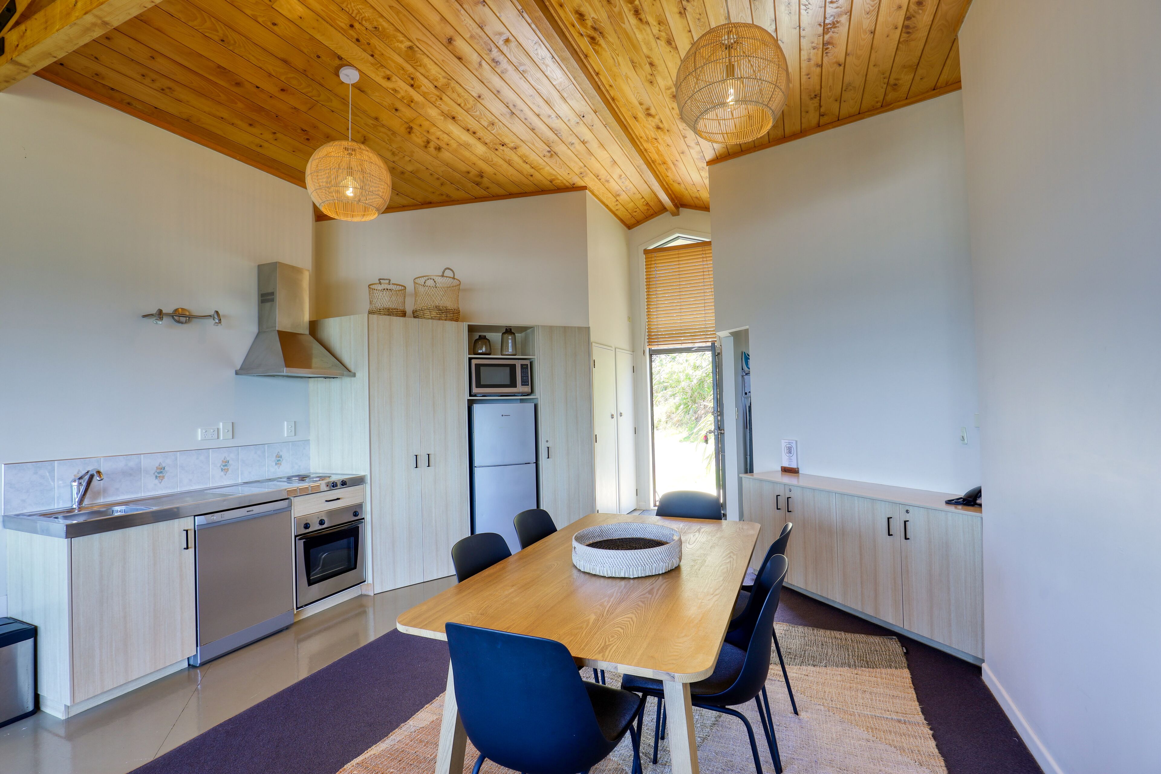 A modern kitchen with wooden ceiling beams, stainless steel appliances, and a dining area with a wooden table and chairs.