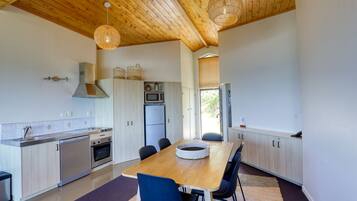 A modern kitchen with wooden ceiling beams, stainless steel appliances, and a dining area with a wooden table and chairs.