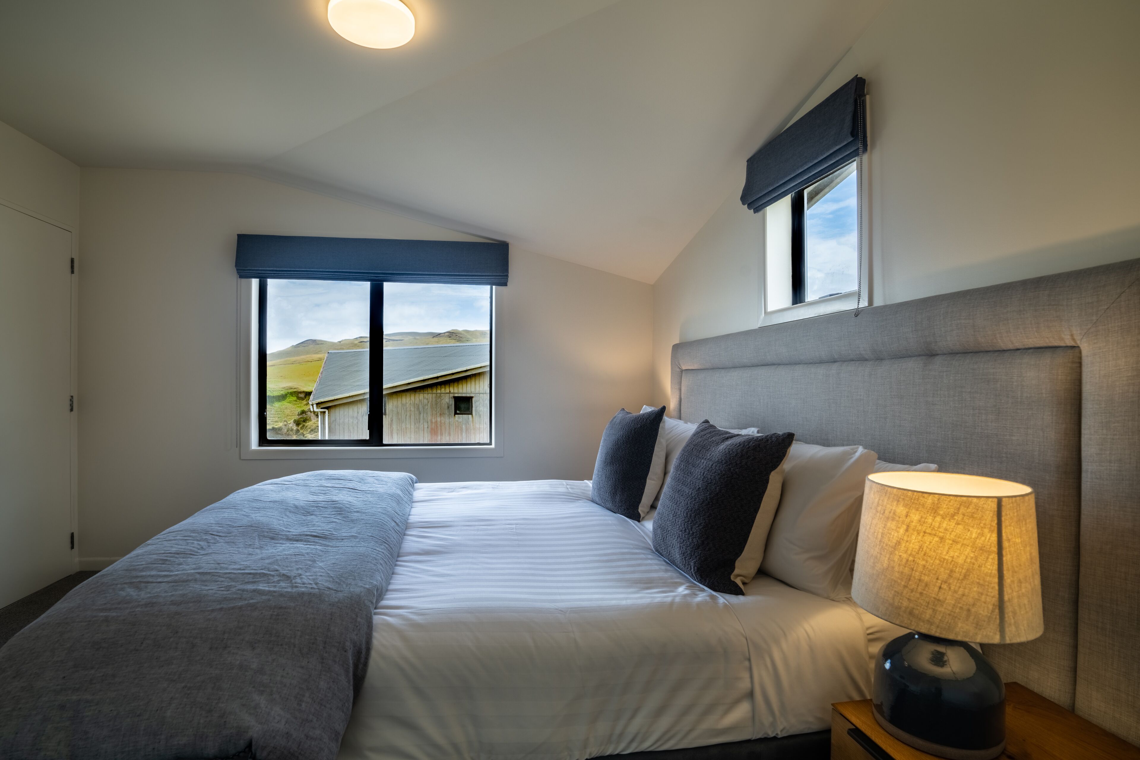 A bedroom with a bed, a nightstand, a lamp, and a window with a view of a landscape.