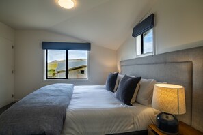 A bedroom with a bed, a nightstand, a lamp, and a window with a view of a landscape.