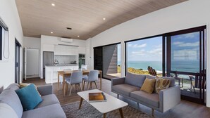 A modern living room with a grey sofa, a coffee table, and a view of the ocean. - Castaways Resort (Lake Puketi)