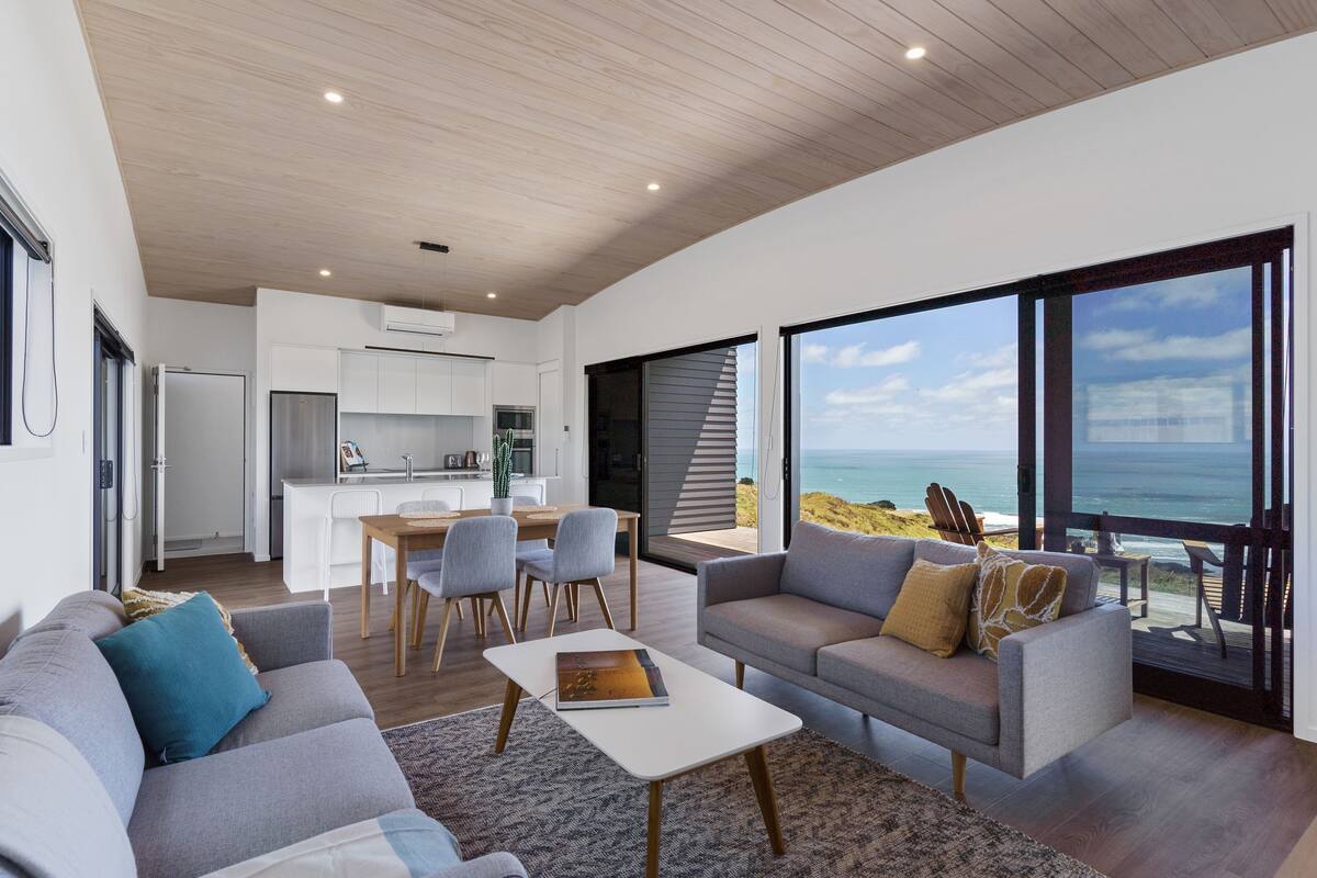 A modern living room with a grey sofa, a coffee table, and a view of the ocean.