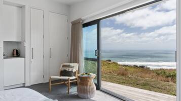 A bedroom with a large sliding glass door leading to a balcony with a view of the ocean.