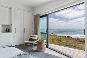 A bedroom with a large sliding glass door leading to a balcony with a view of the ocean. - Castaways Resort (Lake Puketi)