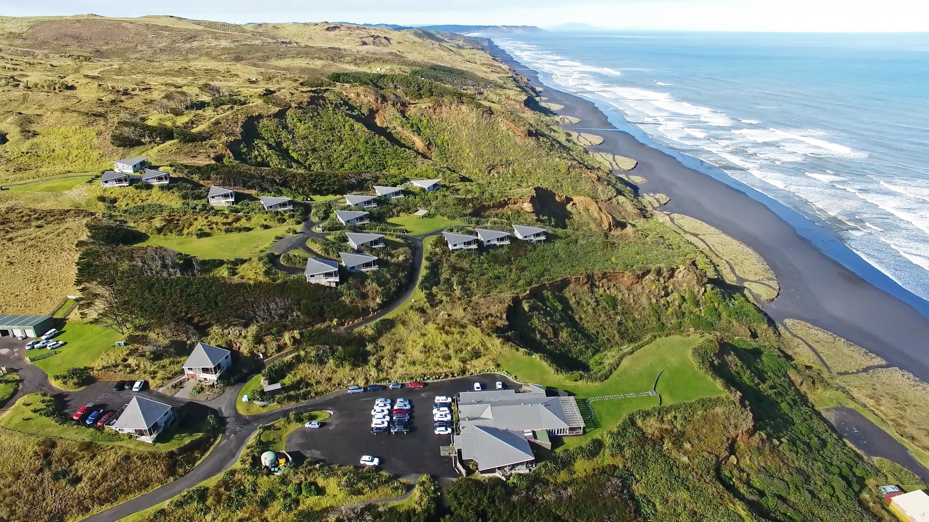 An aerial view of a coastal property with multiple houses, a parking area, and a road leading to the beach.