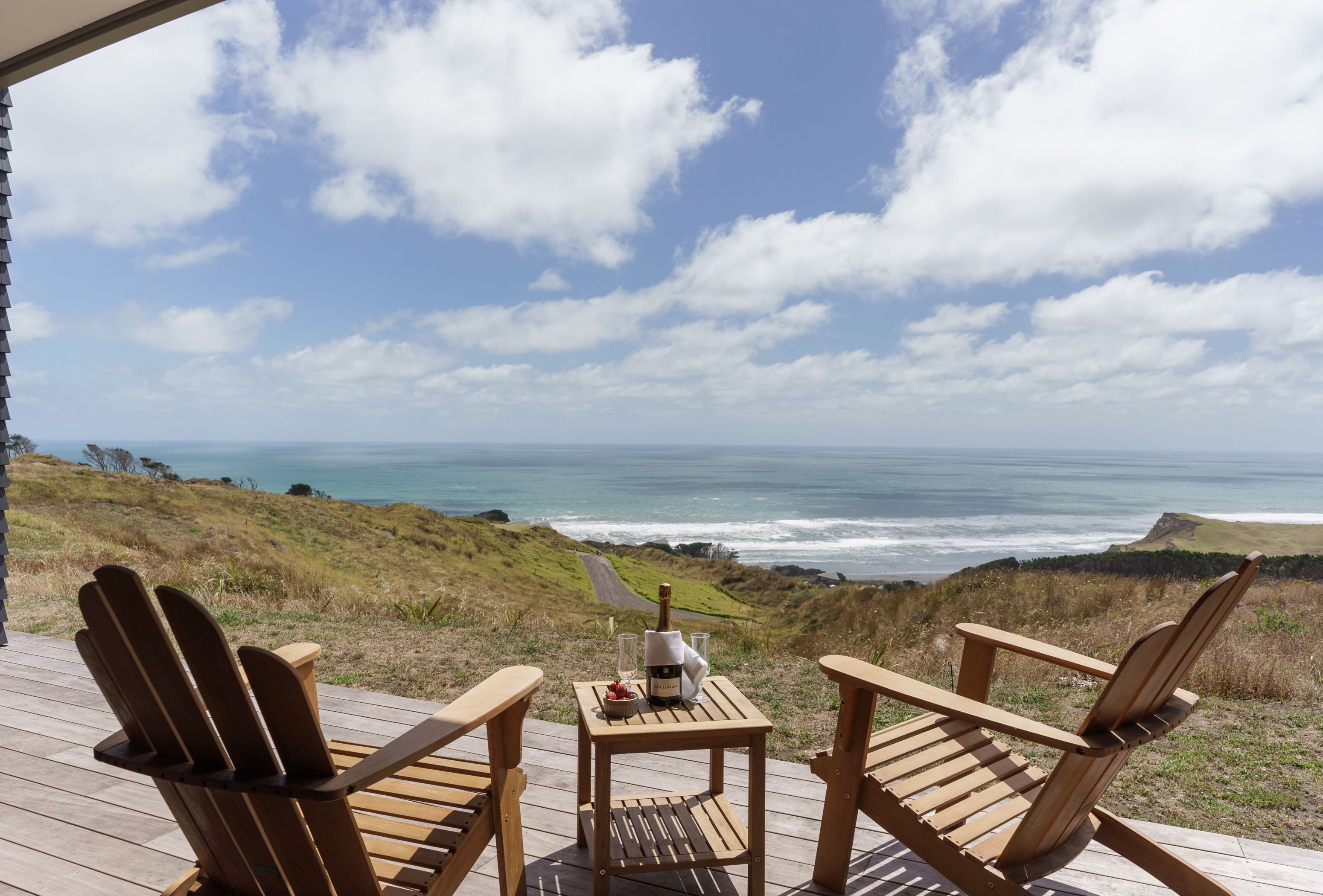 A wooden deck with two Adirondack chairs facing a scenic ocean view.