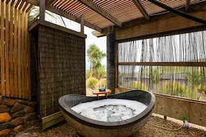A stone hot tub with a wooden bench and a small table, surrounded by a bamboo fence and a stone wall. - Castaways Resort (Lake Puketi)