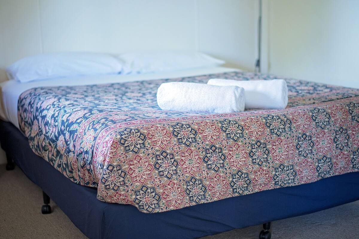 A bed with a patterned bedspread and two rolled towels on it.