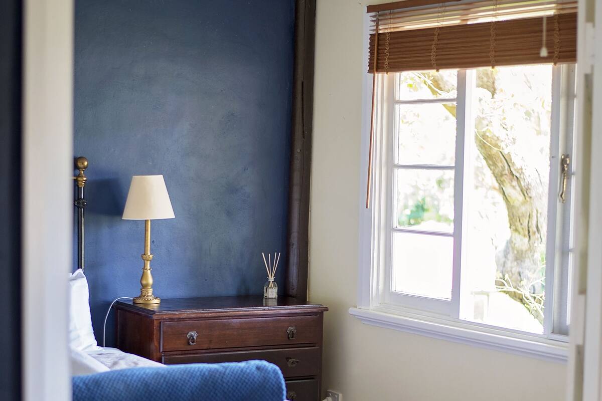 A bedroom with a bed, a nightstand, a lamp, and a window with blinds.