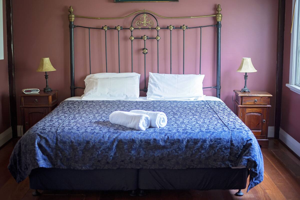 A neatly made bed with a blue patterned bedspread and white pillows, two bedside tables with lamps, and a wooden nightstand with a clock.