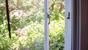 A window with a metal handle, a view of greenery outside, and a door with a latch. - Karribank (Porongurup)