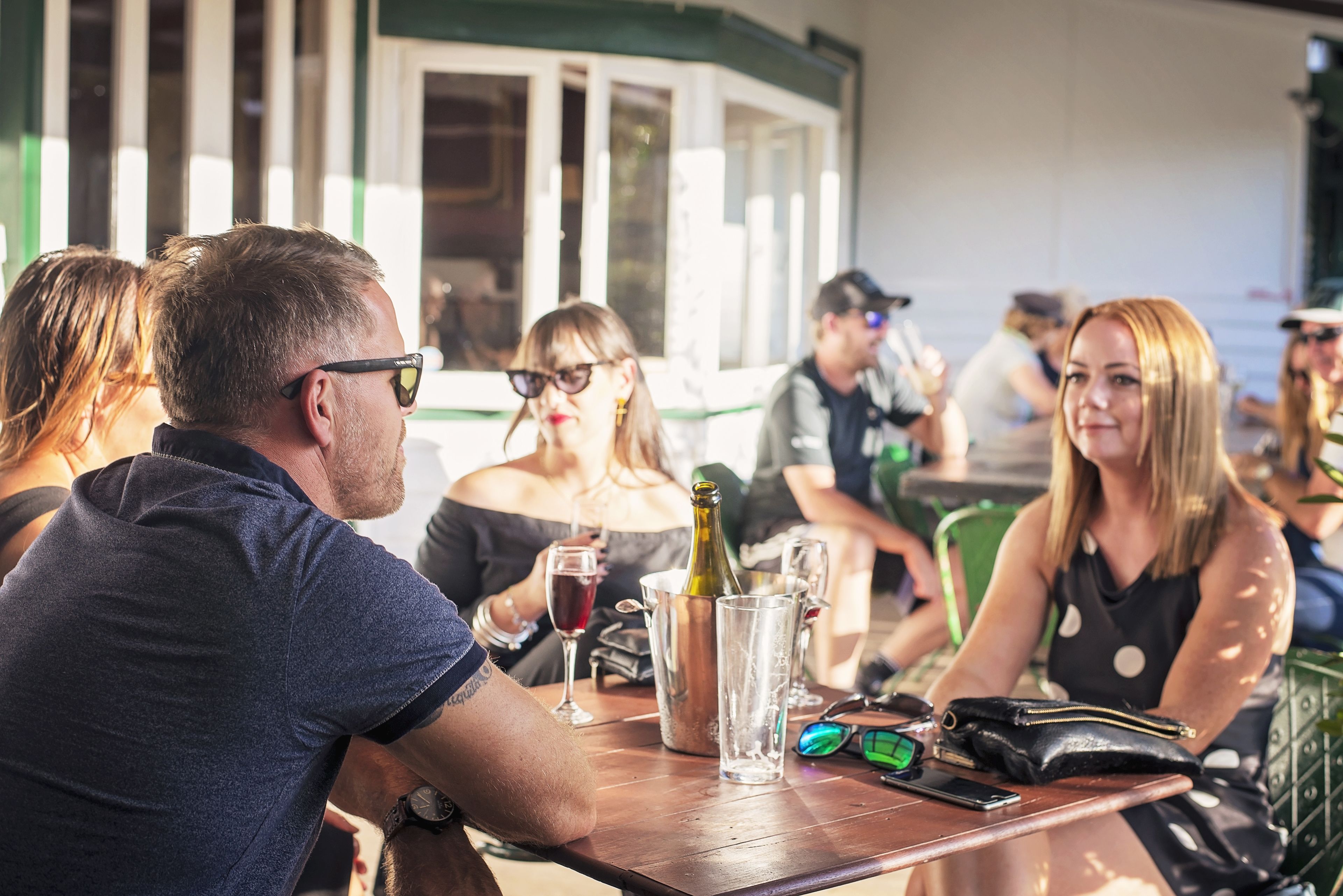 A group of people seated at a wooden table with a bottle of wine, glasses, and a smartphone.