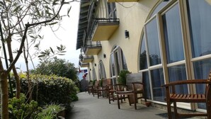 A building with a row of wooden chairs outside, a pathway, and some greenery. - 299 on Devon West (New Plymouth)