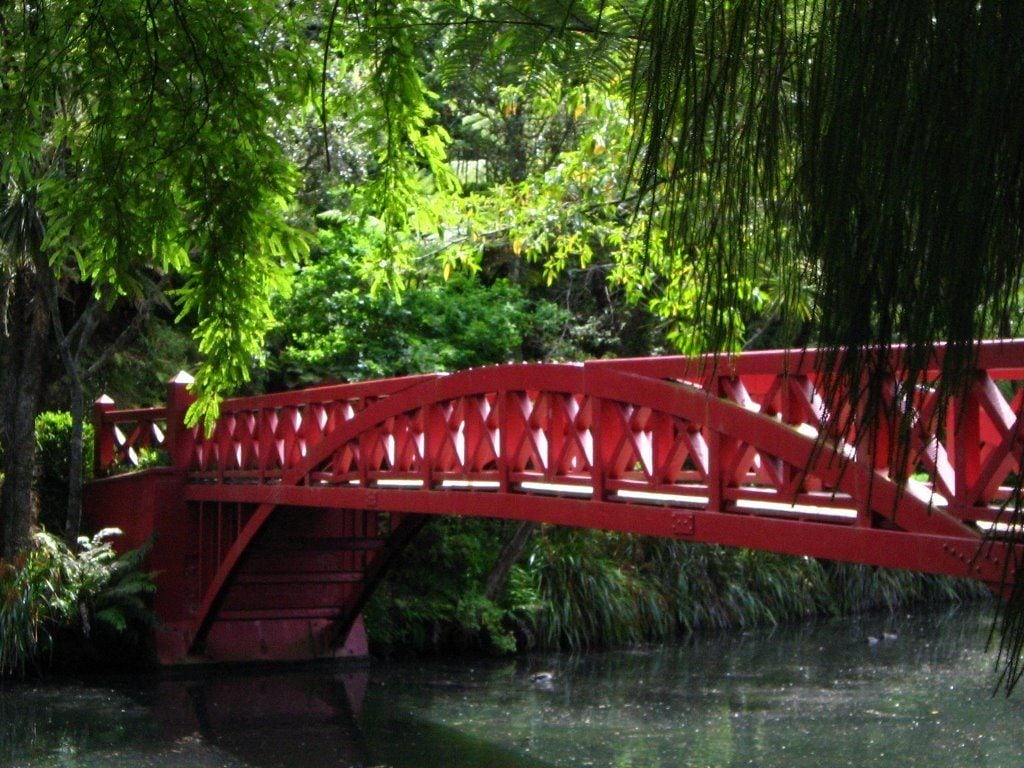 A red bridge over a body of water, surrounded by lush greenery.